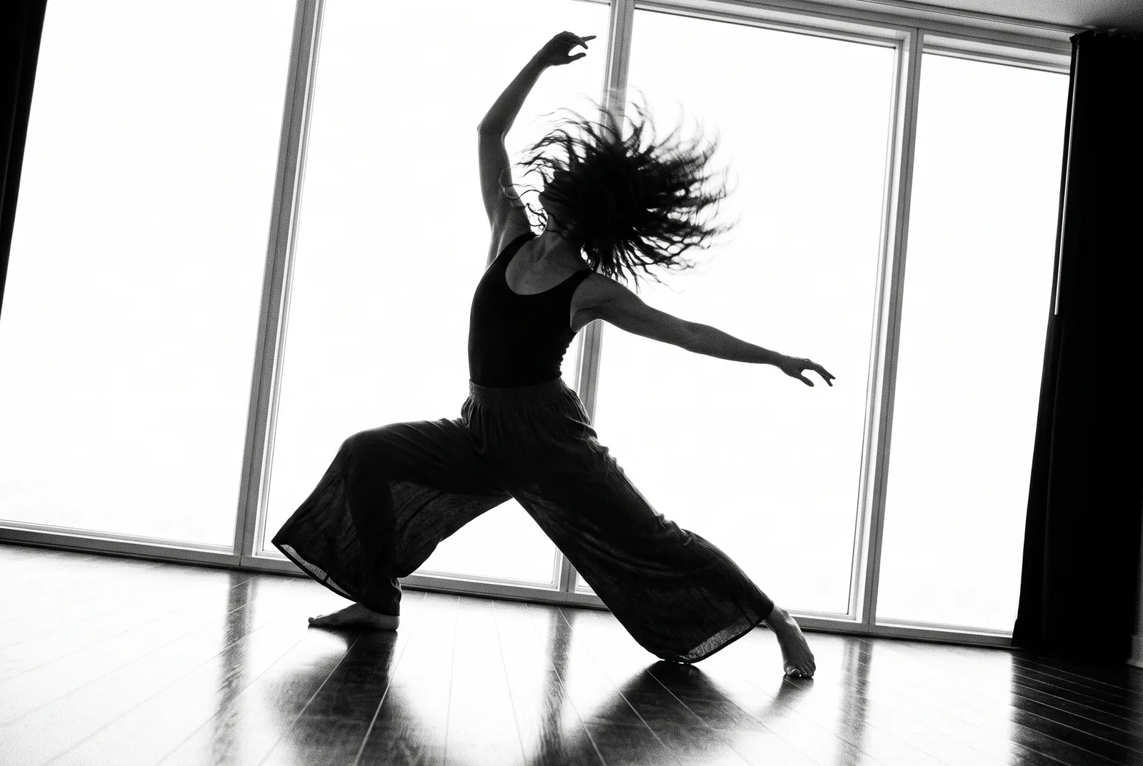 A dancer in silhouette mid hair whip, backlit by bright studio windows